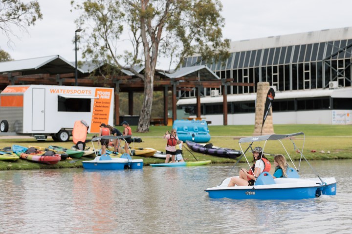 People in pedal boats on a lake near a watersports rental kiosk.