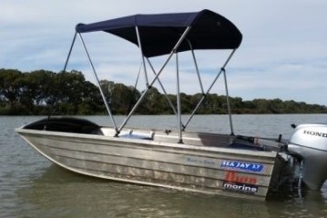 Aluminum boat with a canopy in a calm lake, trees in background.