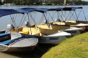 Row of small boats with canopies docked by a riverbank.