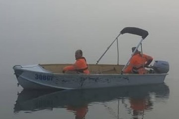 Two people in orange jackets on a small boat in foggy water.