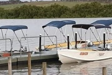 Four small boats with blue canopies moored at a dock on a calm lake.