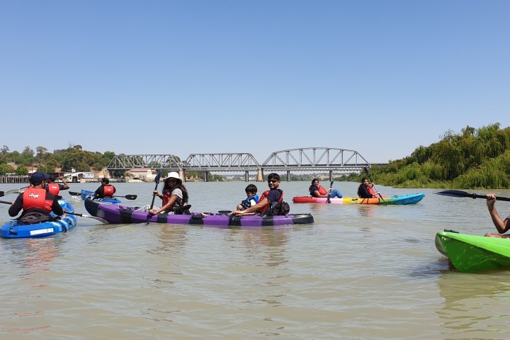 Group kayaking on a river with a bridge in the background.