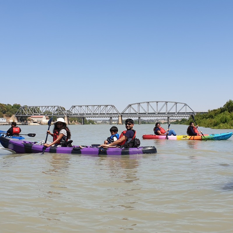 Group kayaking on a river with a bridge in the background.