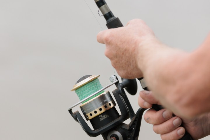Person holding a fishing rod with a spinning reel.