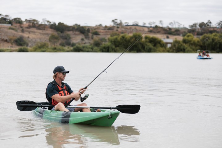 Man in a kayak fishing on a calm river.