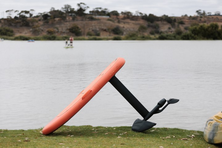 Orange hydrofoil board standing on grass near a calm lake.