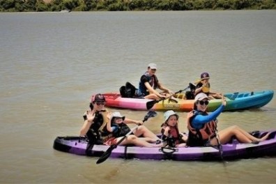 Two colorful kayaks with six people paddling on a calm river.