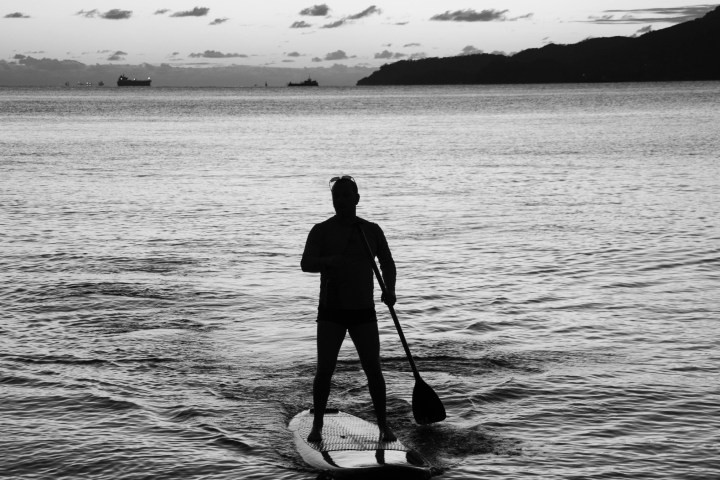 Silhouette of person paddleboarding on calm sea at sunset.