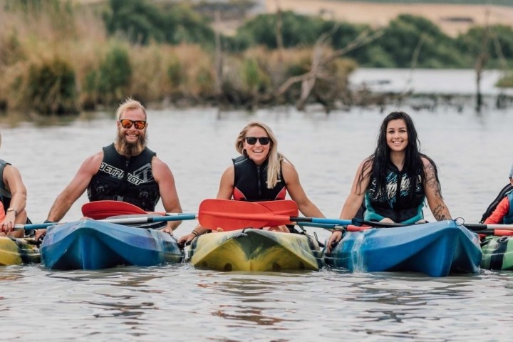 Group of five people in kayaks on a calm lake, smiling.