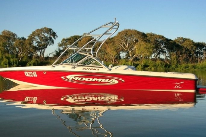 Red and white motorboat on calm water with trees in the background.