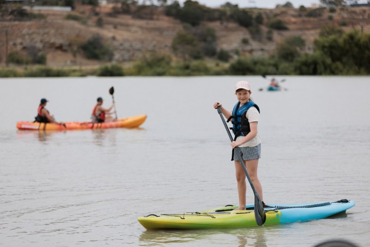 Person paddleboarding on a lake with kayakers in the background.