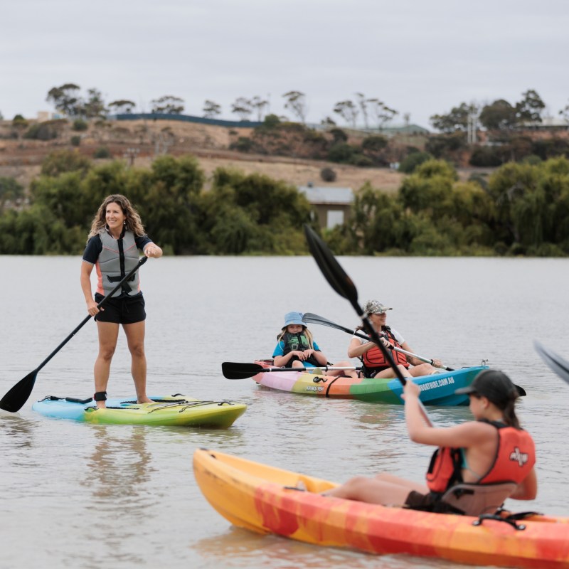 Group kayaking on a calm river with trees in the background.