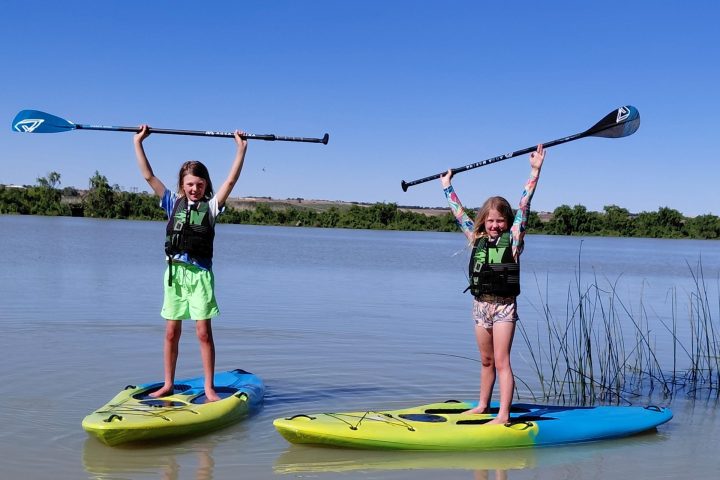 Two people on paddleboards holding paddles upright on a calm lake.