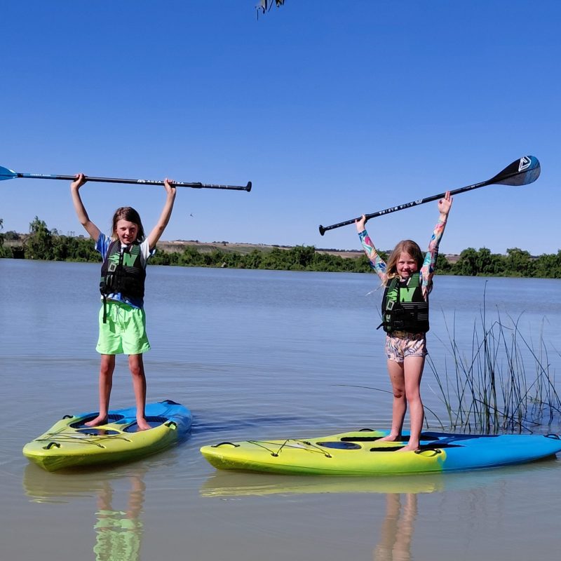 Two people on paddleboards holding paddles upright on a calm lake.