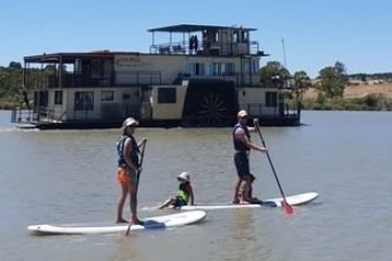 Three people paddleboarding on a river beside a large boat.