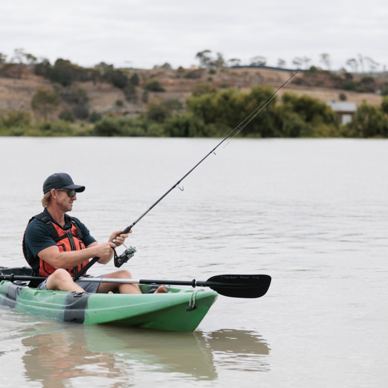 Person fishing from a green kayak on a calm lake.