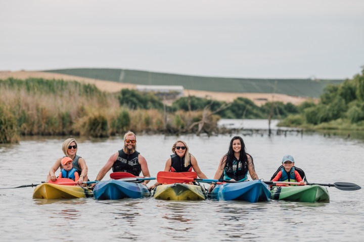 Five people kayaking on a calm river, smiling and wearing life jackets.