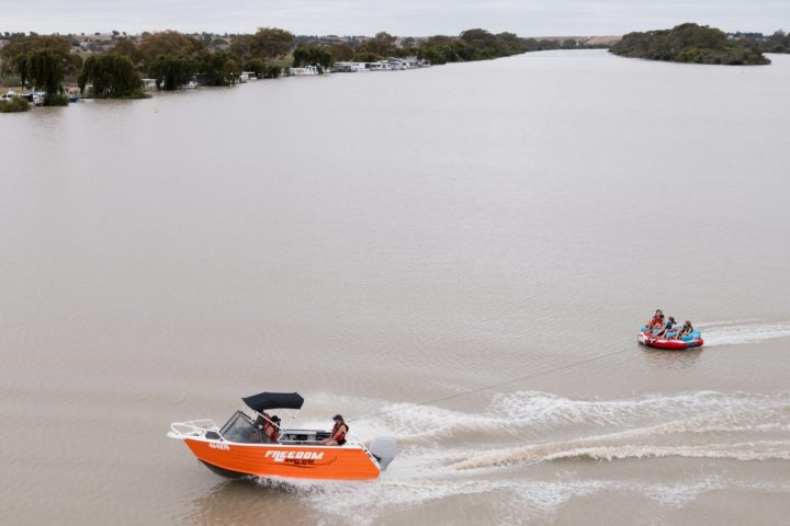 Two boats on a wide river, one towing a tube with people.