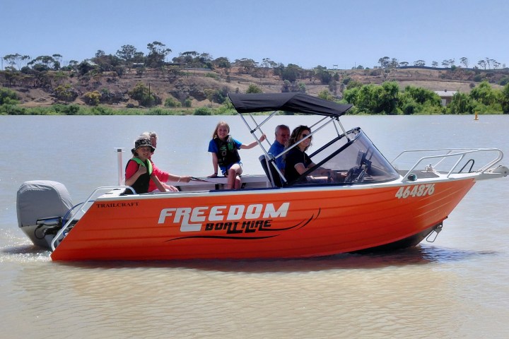 Four people on an orange motorboat named Freedom, cruising on a river.