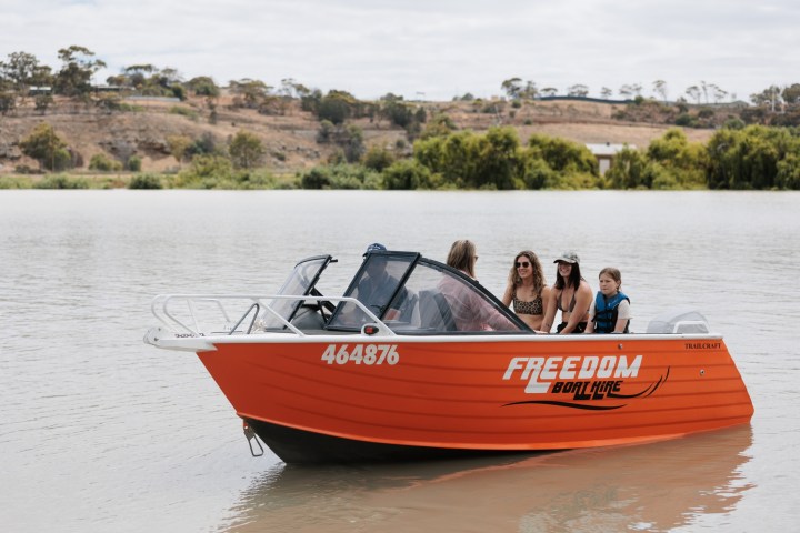 Orange boat with people on a calm river, trees and hills in background.