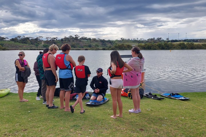 Group of people in life jackets gathered near a lake under cloudy skies.